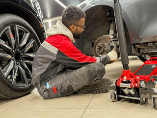 An African-American tire fitter with a wrench in his hands while working. The tire fitter removes...
