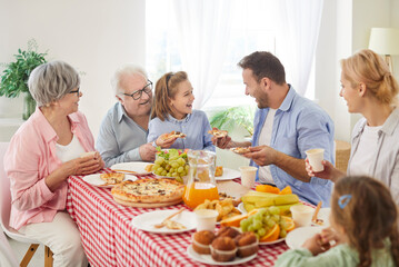 Happy big family gathering eating at table, laughing three generations at meal together at home, enjoying meeting together having fun at party, eating tasty food, parents, grandparents, children