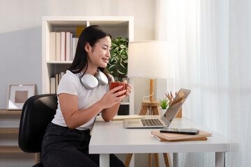 A young girl sits at her desk drinking a hot drink.