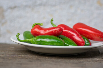 Capsicum annuum Jalapeno chilli hot peppers, group of green and red fruits on wooden brown table on white plate