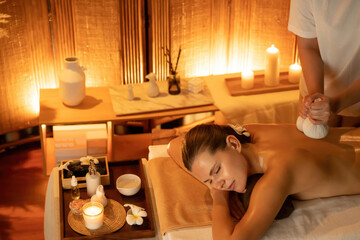 Hot herbal ball spa massage body treatment, masseur gently compresses herb bag on woman body....