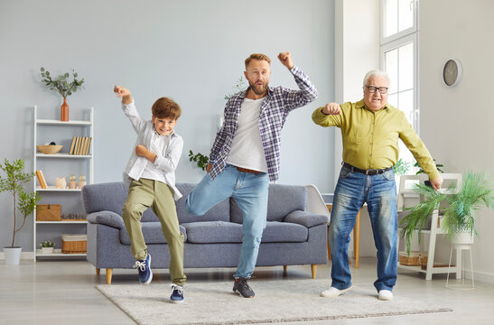 Cheerful multi generation male family having fun together in living room. Happy smiling father, son and grandfather dancing, doing exercises, fooling around and enjoying leisure time. Father Day.