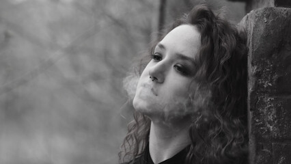 Teen Vaper. Young girl with curly hair smokes an electronic cigarette against a brick wall on the...
