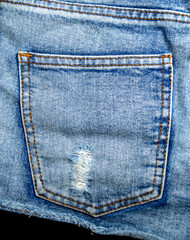 Ripped back pocket on light blue denim jeans close-up showing frayed holes for fashion detail or textile background
