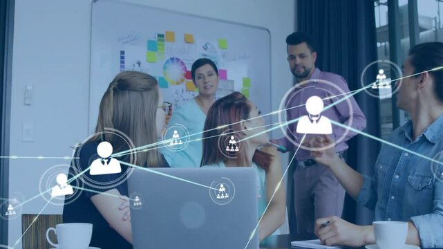 Team collaborating around laptop in business meeting room, showing network icons and sticky notes