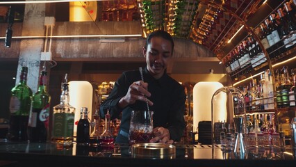 Smart Asian bartender using stirring mixed alcohol syrup into glass with ice for on the rock served...