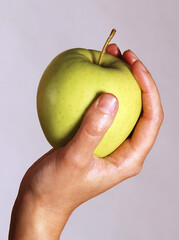A woman's female hand is holding a green apple isolated on a white background. Symbol of well-being and natural health