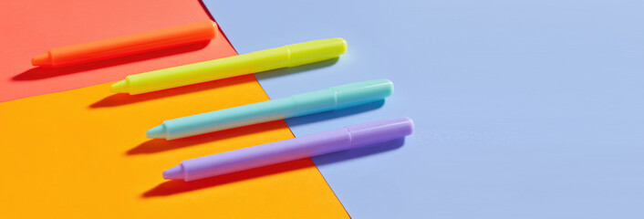 Fototapeta premium Four colorful pens are placed diagonally on a vibrant background with colors red, orange, and blue. Stationery and creativity concept