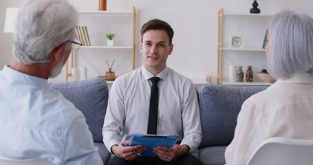 Gray-haired happy smiling senior couple sitting in living room at home and having consultation with a male financial advisor about health insurance. Investment in retirement concept. 4k video.
