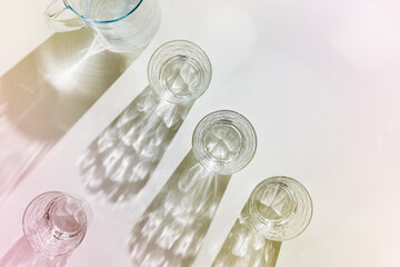 Water Glasses and water jug with Shadows and sunlight Reflection on white background, colored photo minimal style, aesthetic summer still life, refraction throug crystal shine cups, caustics