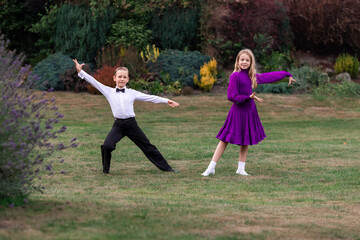 Elegant young boy and girl in ballroom dance attire performing outdoors. This juvenile dance couple...