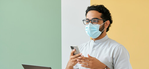 Asian young male in mask holding smartphone in modern office setting