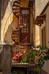 view in alley with steel rusted spiral staircase with shadows in Gythio, Greece