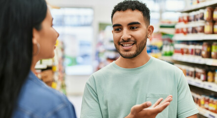 Young hispanic adults engaging in conversation at grocery store aisle