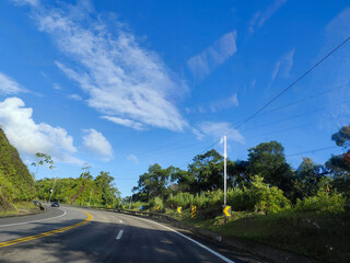 A winding road surrounded by dense rainforest vegetation, with lush green leafy trees, under a...