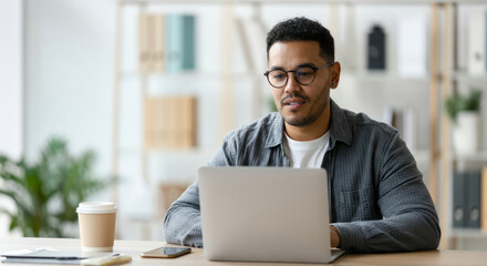 Young hispanic male working on laptop in modern office setting