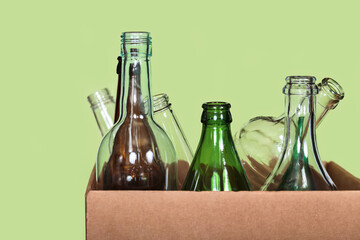 Close front view of cardboard box containing used transparent, green and brown glass bottles on...