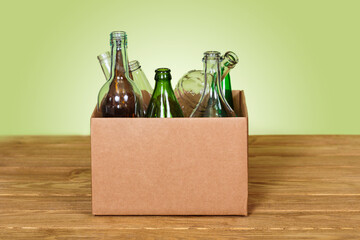 Cardboard box with various glass bottles placed on wooden table against green background