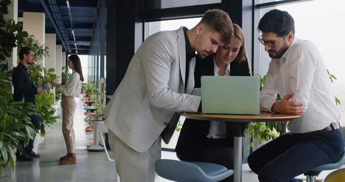 Team of business people meeting in office. Two young men and one woman using laptop computer, working on interesting and successful project, having fun, giving each other high fives. Teamwork concept