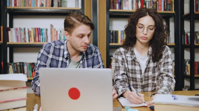 Collaborative study session takes place in a cozy library setting with students focused on their work and discussing ideas near a laptop