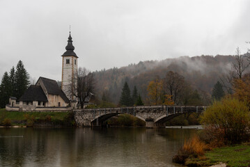 St. John the baptist's church rising from bohinj lake embankment on cloudy autumn day