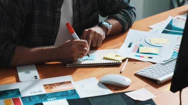 Professional designer writing and designing logo graphic at meeting. Closeup of business man working on colored palettes and writing idea on sticky notes on table with equipment and paper. Symposium.