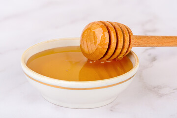 Fresh honey in a white saucer with a wooden honey spoon, close-up.
