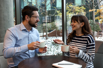 Happy colleagues talking during coffee break at wooden table in cafe