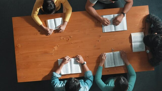 Top view of prayer hold each other support while prays to god at table with bible and cross placed with faith, spirituality and religion. Aerial view of diverse people holding and praying. Symposium.