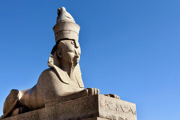 Ancient stone sphinx sculpture with intricate carvings, basking under a clear blue sky, symbolizing...