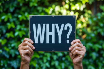 Hands holding a 'WHY?' sign against a leafy background.