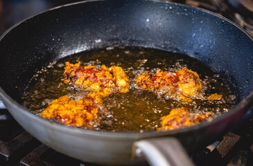 Breaded chicken pieces frying in pan with oil