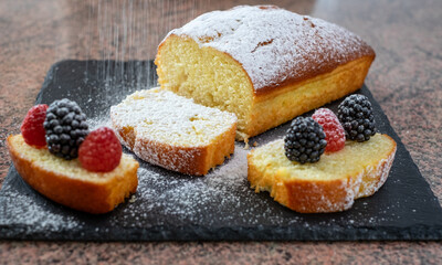 Close-up on the homemade plum cake on a black stone cutting board while being dusted with icing sugar. Cooking at home. Delicious healthy homemade dessert served with berries