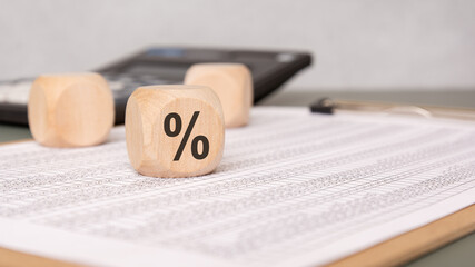 Wooden dice with percentage sign on financial spreadsheet with calculator.