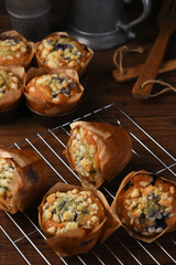 Fresh baked Blueberry Muffins on a cooling rack in a rustic wood kitchen with wooden utensils and metal tea pot.