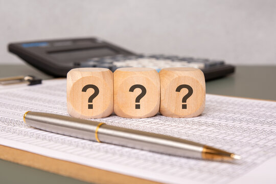 Wooden cubes with question marks on financial documents with pen and calculator