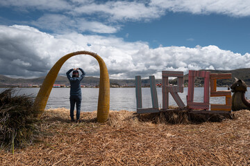 A Girl Standing by the Uros Community Sign on Titicaca Island