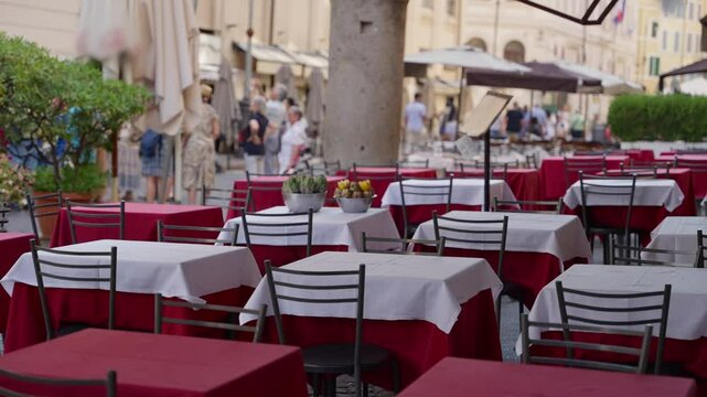 Empty outdoor restaurant tables in busy street summer vacation season in Europe. Locals and tourists walking in hot day in Rome Italy as Italian bistro or cafe waiting for customers with tables ready