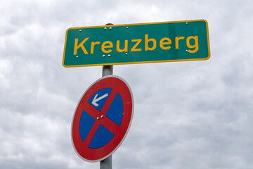 Ortsschild Kreuzberg mit Halteverbotsschild vor bew&ouml;lktem Himmel in Berlin, Deutschland