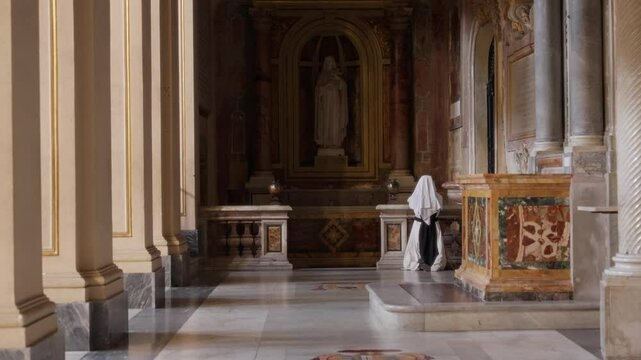Young nun kneeling down in church or cathedral praying by alter or chapel. Female worshiper religious believer nun asking and requesting God in silence inside Catholic building during daytime