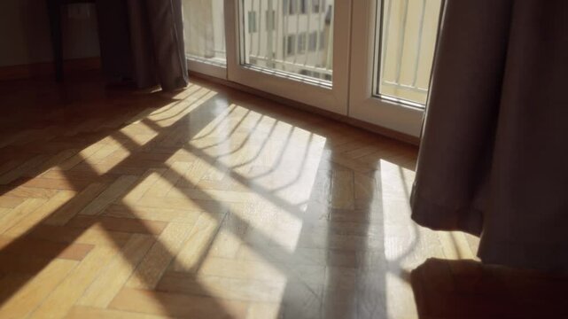 Sun shining through glass window creating shadows on parquet floor in apartment. Light coming in into room in building in European city or town. Bright daylight reflecting from wooden floor in summer