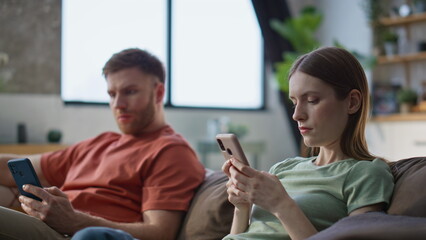Married couple focused mobile phones sitting home couch closeup. Serious spouses
