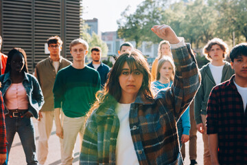 Young woman raising fist during protest march with diverse group of students