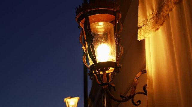 Classic looking street lamps and lantern illuminate dark night with warm light. Close up on two lamps glowing in the dark next to old house or building in Italy in Europe in small historic town
