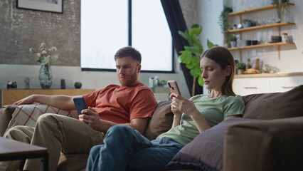 Obraz premium Indifferent couple looking phones sitting home couch. Serious husband wife home