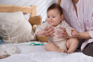 Mother and her cute little baby with rattle toy on bed at home, closeup