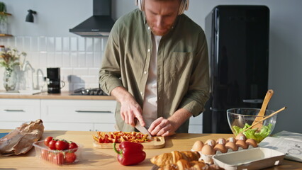 Dancing man slicing vegetables at kitchen countertop in earphones closeup.