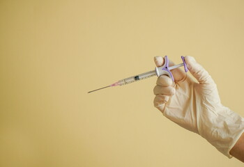 gloved hand holding syringes, against a soft yellow background. Conceptual image related to medicine, beauty injections, or cosmetic procedures