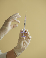 gloved hand holding syringes, against a soft yellow background. Conceptual image related to medicine, beauty injections, or cosmetic procedures