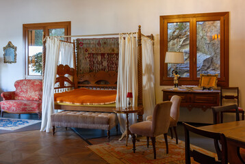 Open-space interior finely decorated with classical-style furniture, with four-poster bed between two windows
